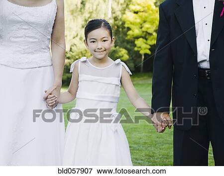 Stock Photo - Asian newlyweds holding flower girl’s hands. Fotosearch