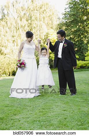Stock Photograph - Asian newlyweds holding flower girl’s hands. Fotosearch