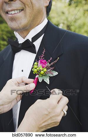 Stock Image - Asian woman pinning groom’s boutonniere. Fotosearch