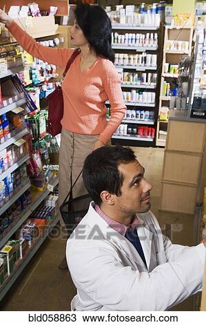 Stock Image - Asian woman shopping next to store clerk . Fotosearch