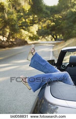 Stock Image - Asian woman’s feet hanging out of convertible car. Fotosearch