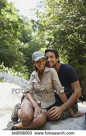 Stock Image - Hispanic couple hugging on rocks. Fotosearch