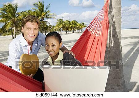 Picture - Hispanic couple with laptop and tropical cocktail. Fotosearch