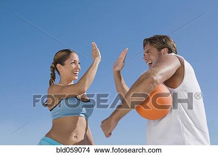 Picture - Hispanic couple with volleyball high-fiving. Fotosearch