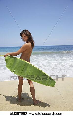 Stock Image - Hispanic woman holding palm frond across buttocks. Fotosearch