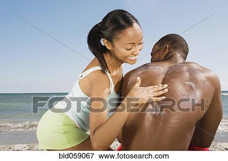Stock Photo - Hispanic woman rubbing sunscreen on boyfriend’s back. Fotosearch