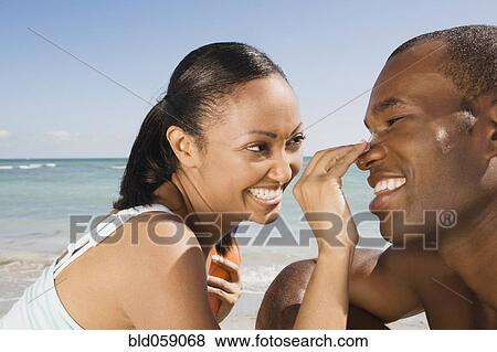 Stock Photo - Hispanic woman rubbing sunscreen on boyfriend’s nose. Fotosearch