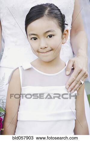 Stock Image - Mixed Race girl standing in front of bride. Fotosearch