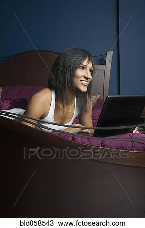Mixed Race woman with laptop on bed View Large Photo Image Stock Image - Mixed Race woman with laptop on bed. Fotosearch