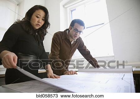 Stock Image - Multi-ethnic businesspeople looking at blueprints. Fotosearch