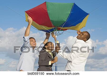 Stock Image - Multi-ethnic businesspeople opening beach umbrella. Fotosearch