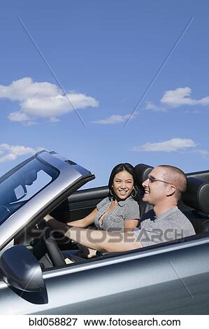 Stock Photo - Multi-ethnic couple driving in convertible car. Fotosearch