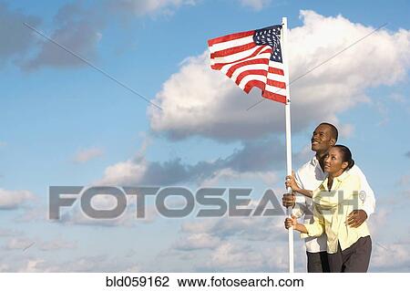 Stock Image - Multi-ethnic couple holding American flag. Fotosearch