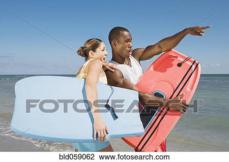 Stock Image - Multi-ethnic couple holding bodyboards. Fotosearch