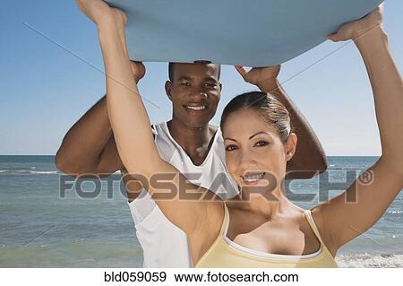 Multi-ethnic couple holding boogie board View Large Photo Image Stock Photo - Multi-ethnic couple holding boogie board. Fotosearch