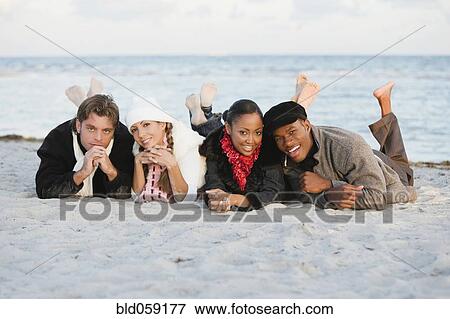 Stock Photo - Multi-ethnic couples laying on beach. Fotosearch