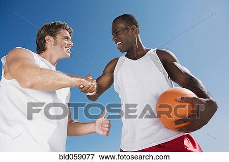 Stock Photo - Multi-ethnic men with volleyball shaking hands. Fotosearch