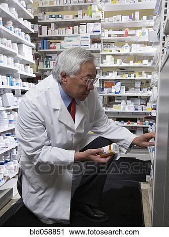Stock Image - Senior Asian pharmacist looking at medication. Fotosearch