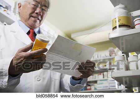 Picture - Senior Asian pharmacist reading prescription. Fotosearch