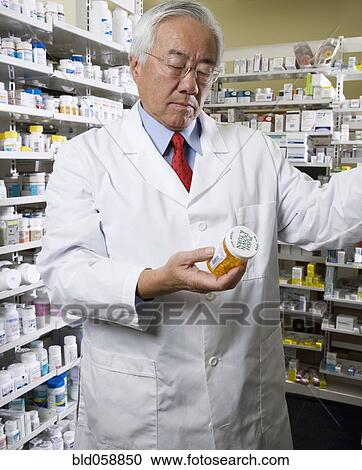 Stock Image - Senior Asian pharmacist reading medication. Fotosearch
