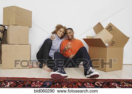 Stock Image - African couple with wine next to moving boxes. Fotosearch