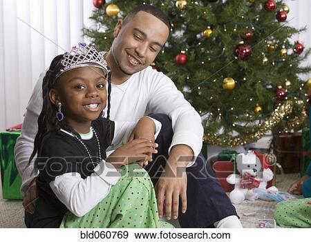 Stock Photo - African father and daughter in front of Christmas tree. Fotosearch