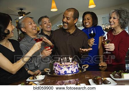 Stock Image - African man celebrating birthday with multi-ethnic friends. Fotosearch
