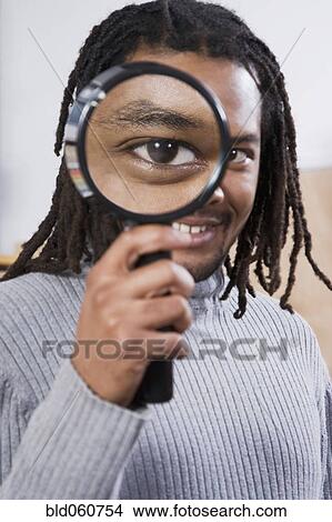 Picture - African man looking through magnifying glass. Fotosearch