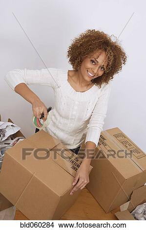 Picture - African woman taping moving box. Fotosearch