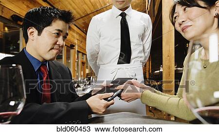 Stock Image - Asian couple fighting over restaurant bill. Fotosearch