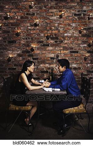 Stock Image - Asian couple holding hands at restaurant. Fotosearch