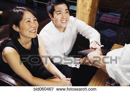 Stock Photo - Asian couple paying restaurant bill. Fotosearch