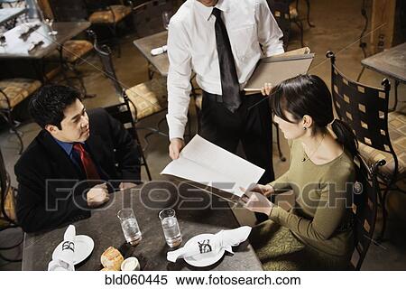 Stock Photography - Asian couple reading menu at restaurant. Fotosearch