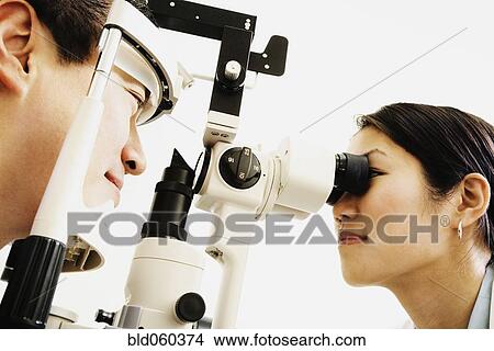 Picture - Asian female optometrist examining patient. Fotosearch