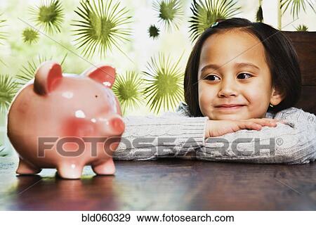 Stock Photo - Asian girl looking at piggy bank. Fotosearch
