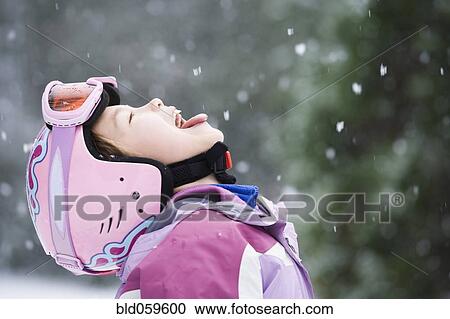 Stock Image - Asian girl sticking out tongue in snow. Fotosearch