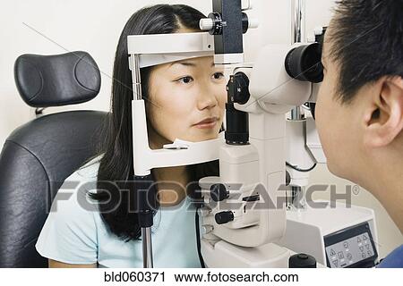 Stock Image - Asian male optometrist examining patient. Fotosearch