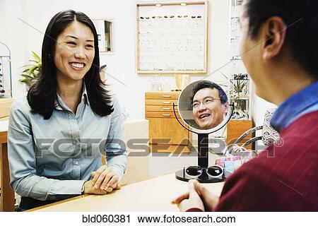 Stock Image - Asian optician assisting customer. Fotosearch