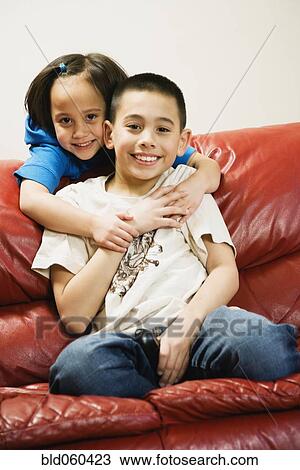 Stock Image - Asian siblings hugging on sofa. Fotosearch