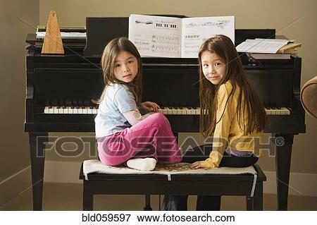 Stock Photo - Asian sisters sitting at piano. Fotosearch