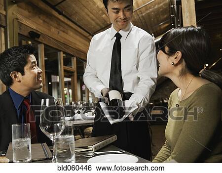 Stock Photograph - Asian waiter showing wine to couple. Fotosearch