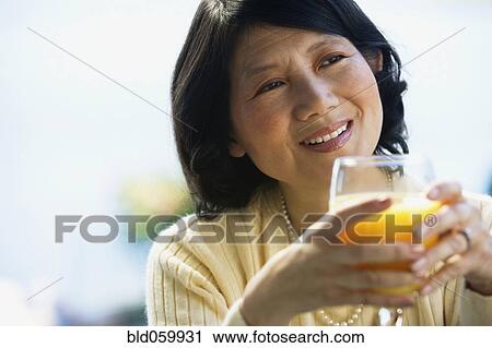 Stock Image - Asian woman drinking orange juice. Fotosearch
