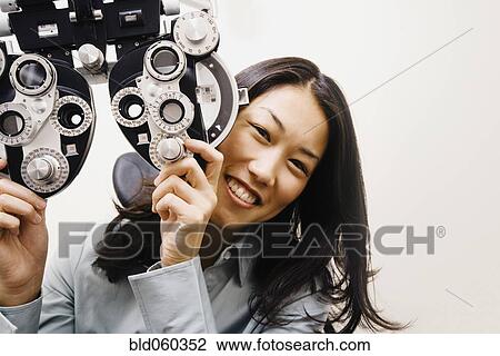 Stock Image - Asian woman next to ophthalmic refractor. Fotosearch