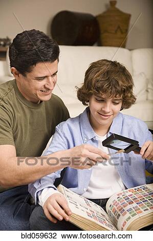 Stock Image - Hispanic father and son examining stamp through magnifying glass. Fotosearch