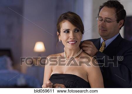 Stock Image - Hispanic man fastening wife’s necklace. Fotosearch