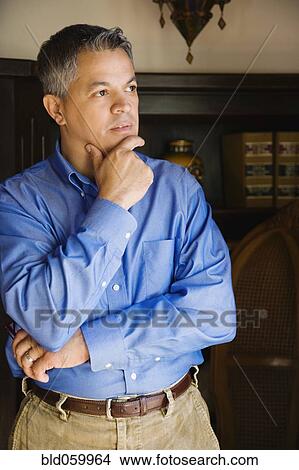 Picture - Hispanic man thinking with hand on chin. Fotosearch