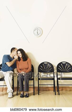 Stock Photo - Multi-ethnic couple telling secret in waiting area. Fotosearch