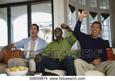 Multi-ethnic men cheering on sofa View Large Photo Image Picture - Multi-ethnic men cheering on sofa. Fotosearch