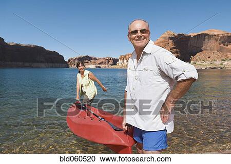Stock Image - Multi-ethnic senior couple carrying kayak. Fotosearch