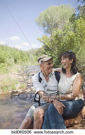 Stock Photograph - Multi-ethnic senior couple hugging next to stream. Fotosearch